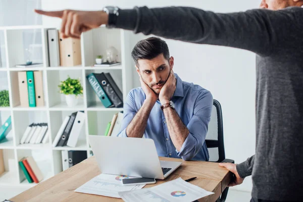 Selective focus of african american businessman pointing with finger near sad collage at table in office — Stock Photo