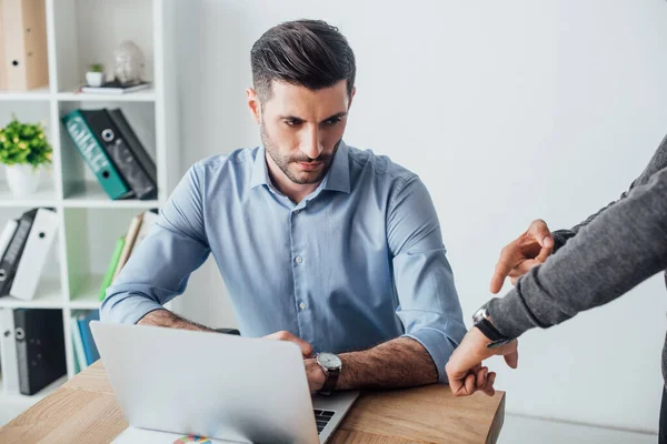 Businessman pointing at wristwatch to colleague near laptop on table in office — Stock Photo