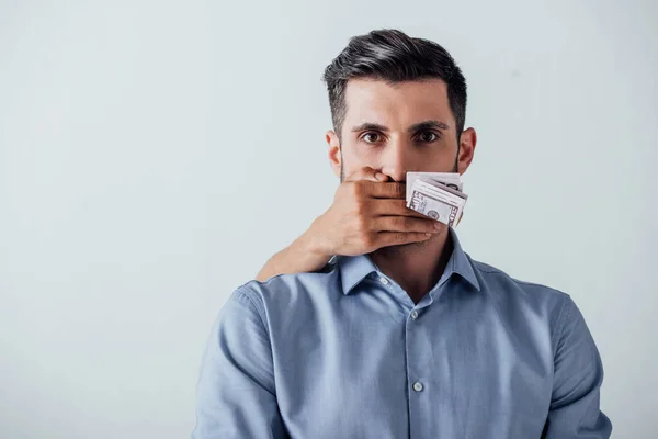 Billets libellés en dollars détenus à la main par un homme et couvrant la bouche de l'homme isolé sur gris — Photo de stock