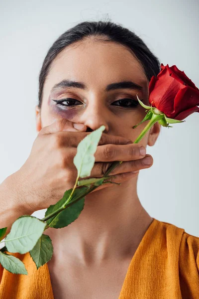 Male hand covering mouth to indian woman with bruise while holding rose isolated on grey — Stock Photo