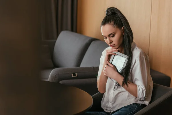 Selective focus of depressed young woman holding photo frame near chest — Stock Photo