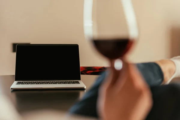 Foyer sélectif de la femme tenant verre de vin rouge près d'un ordinateur portable avec écran blanc — Photo de stock
