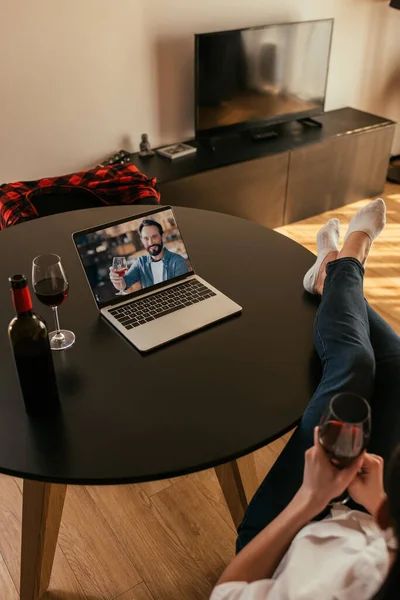 Обрізаний вид жінки і молодого чоловіка на екрані ноутбука, що тримає окуляри червоного вина — стокове фото