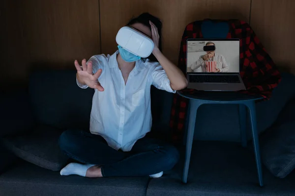 Mujer joven extendiendo la mano, y el novio en la pantalla de la computadora portátil comer palomitas de maíz mientras se utilizan auriculares vr juntos - foto de stock