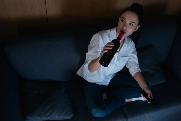 Alta visão anjo de mulher deprimida bebendo vinho de garrafa enquanto sentado no sofá — Fotografia de Stock