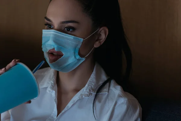 Young woman with hole in medical mask drinking soda while watching tv at home — Stock Photo