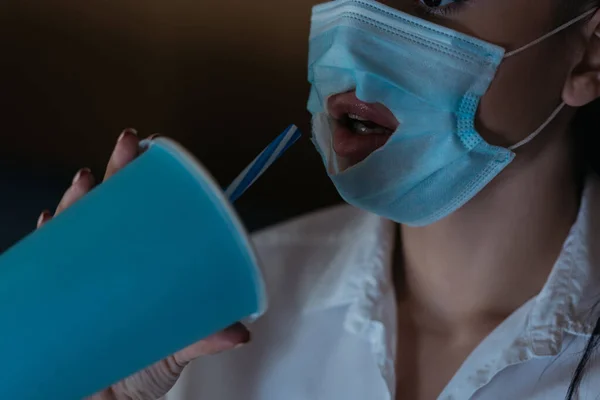 Cropped view of young woman drinking soda through hole in medical mask — Stock Photo