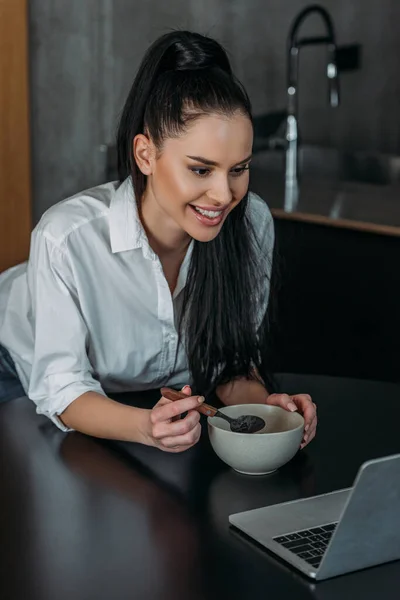 Smiling woman having breakfast during video chat on laptop — Stock Photo