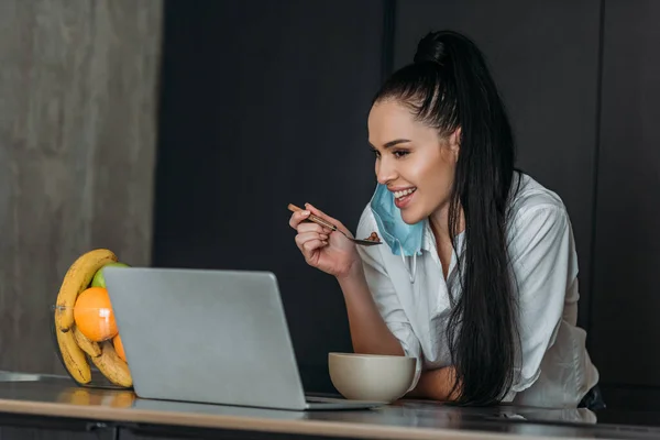 Улыбающаяся женщина держит ложку во время видео чата на ноутбуке — стоковое фото