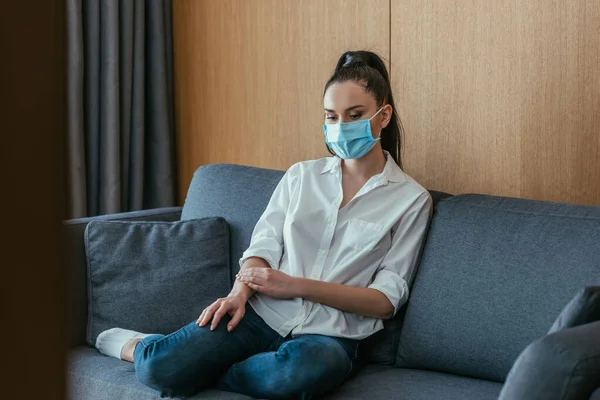 Solitario, sconvolto giovane donna in maschera protettiva seduta sul divano a casa — Foto stock