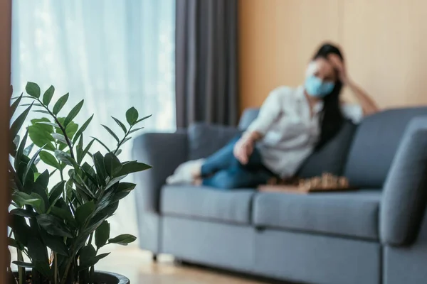 Selective focus of depressed woman in medical mask sitting near chessboard — Stock Photo