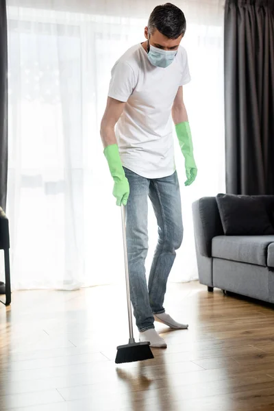 Человек в медицинской маске моет пол в гостиной — стоковое фото