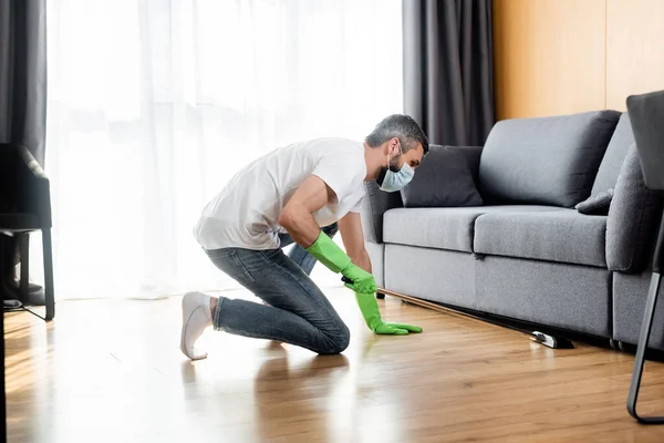 Вид збоку чоловіка в медичній масці для прибирання підлоги вдома — стокове фото