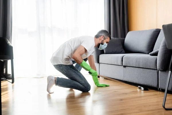 Seitenansicht eines Mannes in medizinischer Maske, der zu Hause den Fußboden reinigt — Stockfoto