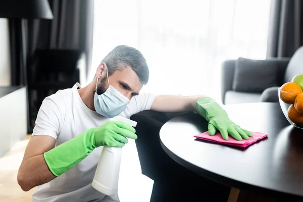 Uomo in maschera medica tavolo di pulizia in soggiorno — Foto stock