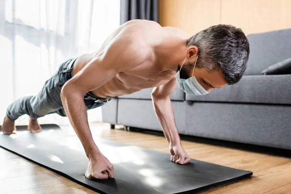 Homem muscular em máscara médica fazendo flexões no tapete de fitness em casa — Fotografia de Stock