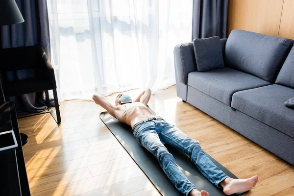 Shirtless man in medical mask lying on fitness mat in living room — Stock Photo