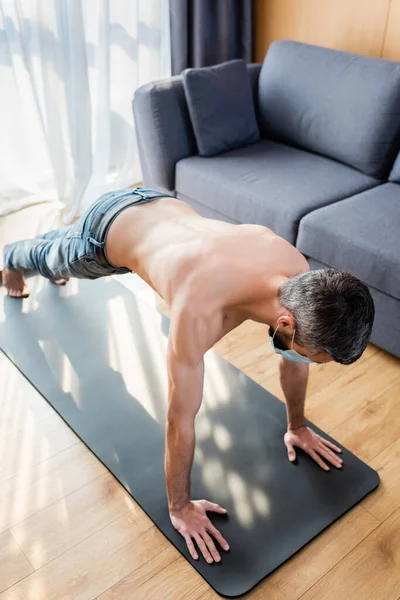 Mann mit medizinischer Maske trainiert zu Hause auf Fitnessmatte — Stockfoto