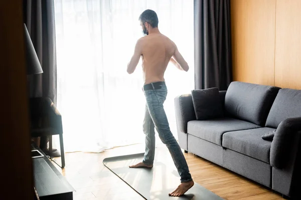 Hombre sin camisa en el entrenamiento de la máscara médica en la estera de fitness en la sala de estar - foto de stock