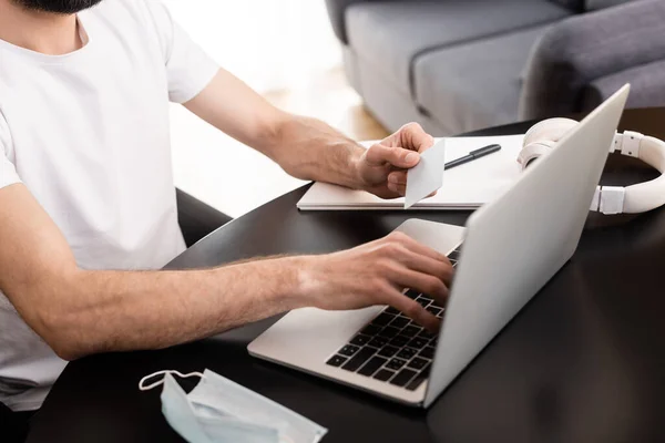 Vista recortada do freelancer usando laptop e cartão de crédito perto de máscara médica na mesa — Fotografia de Stock