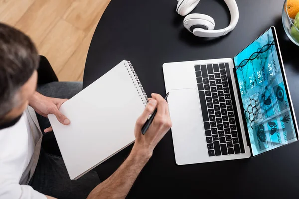 Overhead view of man holding notebook near laptop with e health website on screen — Stock Photo