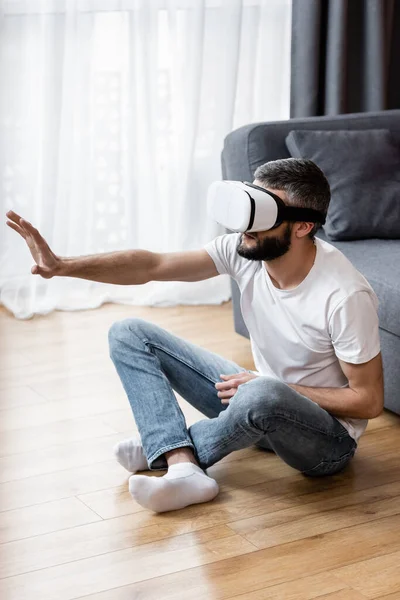 Homem usando fone de ouvido de realidade virtual enquanto sentado no chão em casa — Fotografia de Stock