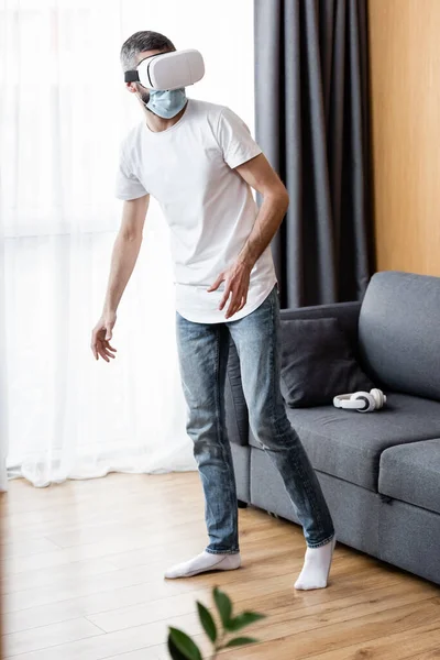 Foco seletivo do homem em máscara médica usando fones de ouvido vr em casa — Fotografia de Stock