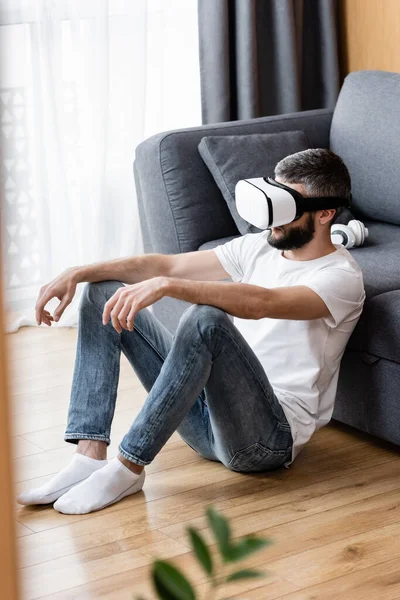 Selective focus of man in vr headset sitting near couch on floor — Stock Photo