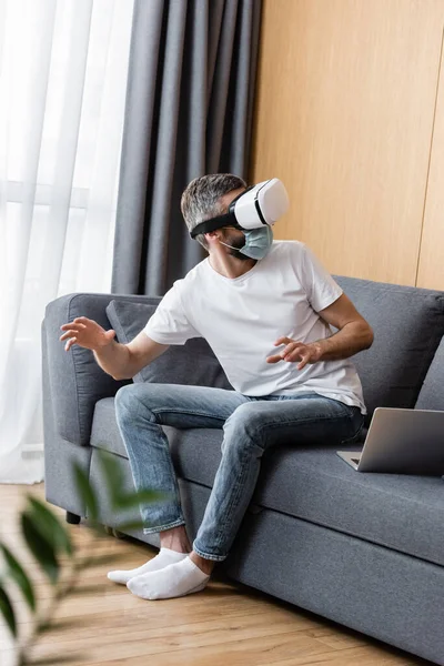 Вибірковий фокус людини в медичній масці за допомогою гарнітури vr на дивані у вітальні — Stock Photo