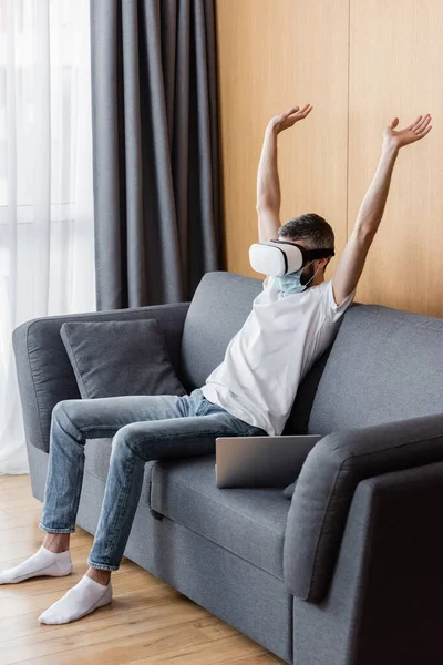 Человек в медицинской маске и гарнитуре сидит дома на диване — стоковое фото