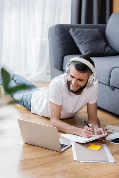 Enfoque selectivo del hombre sonriente en auriculares usando computadora portátil y papelería durante la educación en línea en el hogar - foto de stock