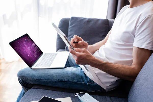 Vista recortada de la escritura freelancer en el cuaderno cerca del ordenador portátil con e sitio web de salud en la pantalla - foto de stock