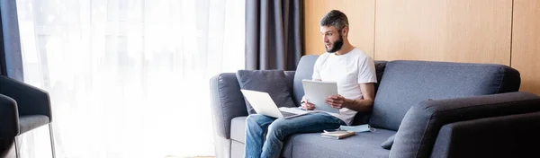 Ausschnitt eines Telearbeiters, der sein Notizbuch hält, während er mit Laptop in der Nähe der medizinischen Maske auf der Couch arbeitet — Stockfoto
