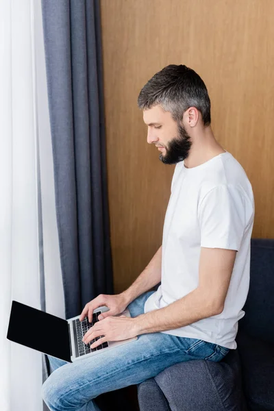 Side view of teleworker using laptop on sofa at home — Stock Photo