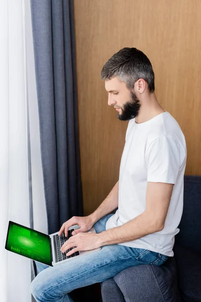 Vista laterale dell'uomo utilizzando laptop con grafici e grafici sullo schermo in soggiorno — Foto stock