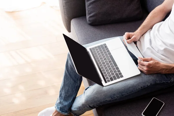 Cropped view of freelancer holding medical mask near laptop and smartphone on couch — Stock Photo