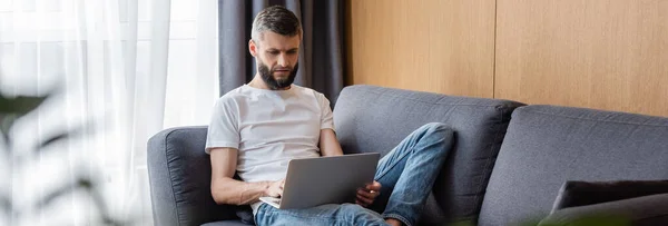 Panoramic orientation of handsome teleworker using laptop in living room — Stock Photo