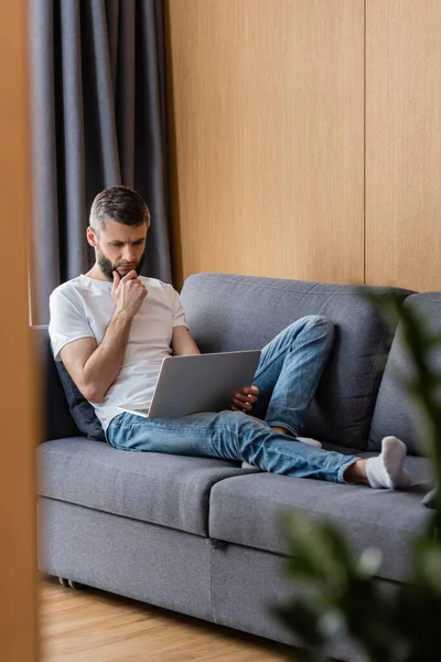 Selective focus of freelancer using laptop while working on couch in living room — Stock Photo