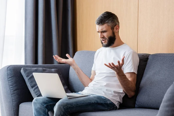 Confused freelancer looking at laptop while sitting on couch at home — Stock Photo