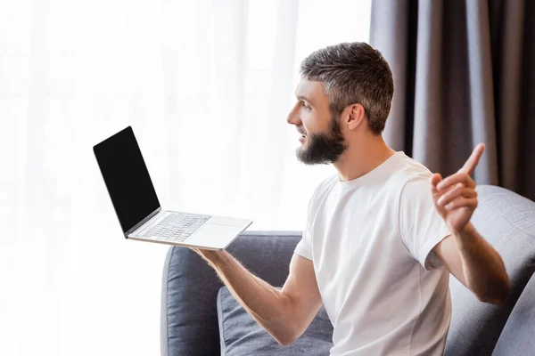 Vista lateral do freelancer apontando com o dedo enquanto conversa por vídeo no laptop em casa — Fotografia de Stock