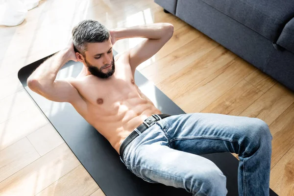 Vista de ángulo alto del hombre musculoso haciendo abdominales mientras hace ejercicio en la estera de fitness en casa - foto de stock
