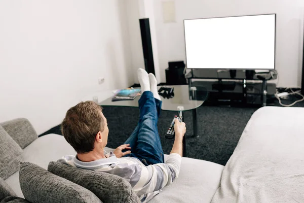 Человек в джинсах, держащий пульт дистанционного управления возле белого экрана телевизора дома — стоковое фото
