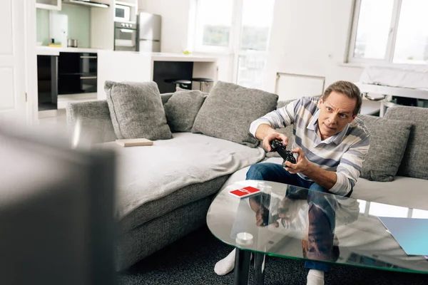 KYIV, UKRAINE - APRIL 14, 2020: selective focus of man playing video game and holding joystick near smartphone with youtube app on coffee table — Stock Photo