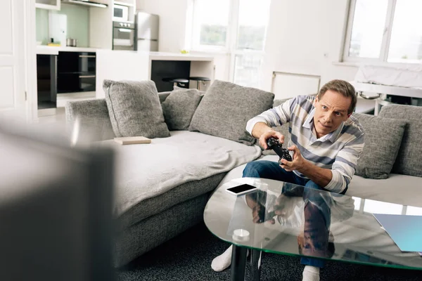 KYIV, UKRAINE - APRIL 14, 2020: selective focus of man playing video game and holding joystick near smartphone with blank screen on coffee table — Stock Photo