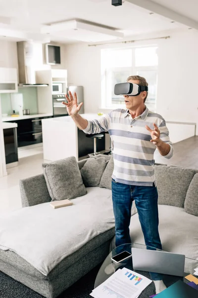 Surprised man in virtual reality headset gesturing at home — Stock Photo