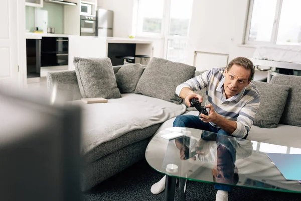 KYIV, UCRANIA - 14 DE ABRIL DE 2020: enfoque selectivo del hombre jugando a videojuegos y sosteniendo el joystick cerca del teléfono inteligente con pantalla blanca en la mesa de café - foto de stock