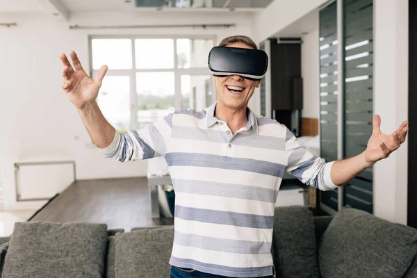 Hombre feliz en auriculares de realidad virtual con las manos extendidas en casa - foto de stock