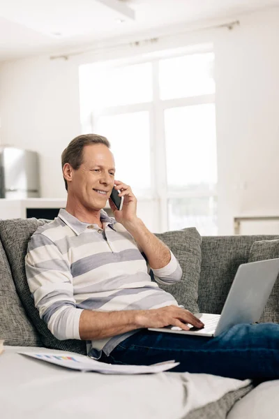 Foyer sélectif de freelance joyeux parler sur smartphone et en utilisant un ordinateur portable à la maison — Photo de stock