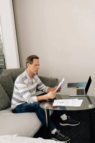 Freelancer looking at charts and graphs while working from home near laptop — Stock Photo