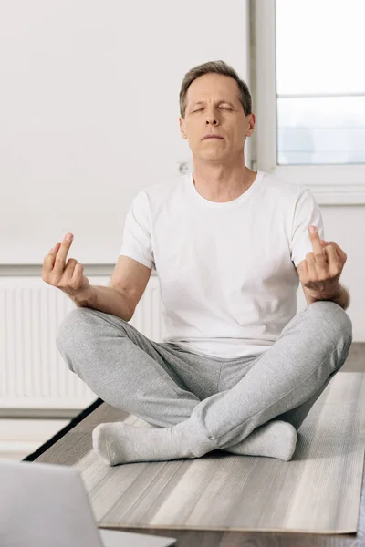 Hombre en calcetines sentado en pose de loto y mostrando los dedos medios - foto de stock